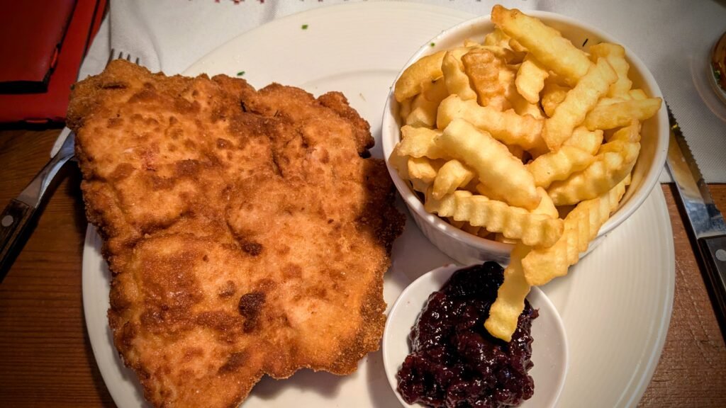 a plate of wiener schnitzel with fries and cranberry sauce