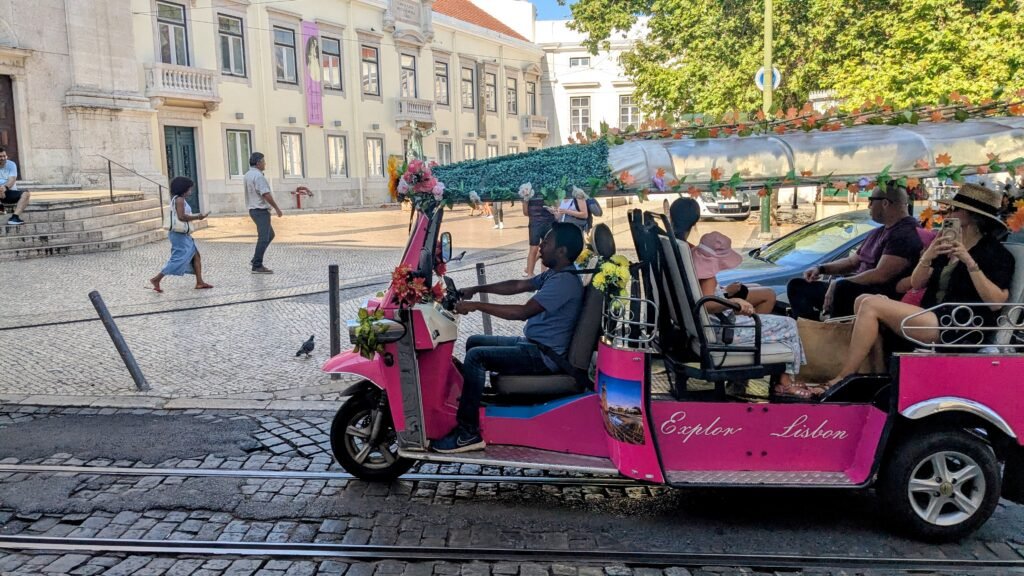 a pink tuk tuk driving along a street in downtown lisbon