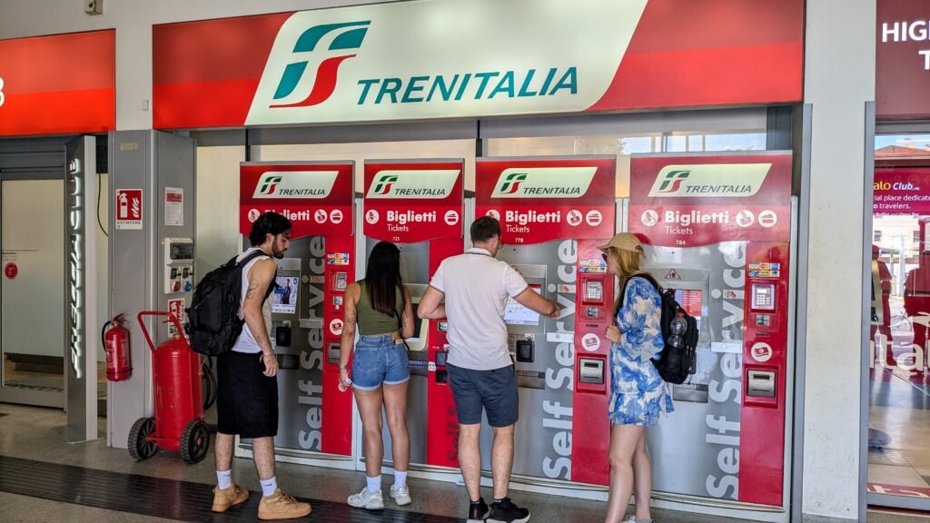 people buying tickets from a trenitalia ticket machine at bologna train station in italy