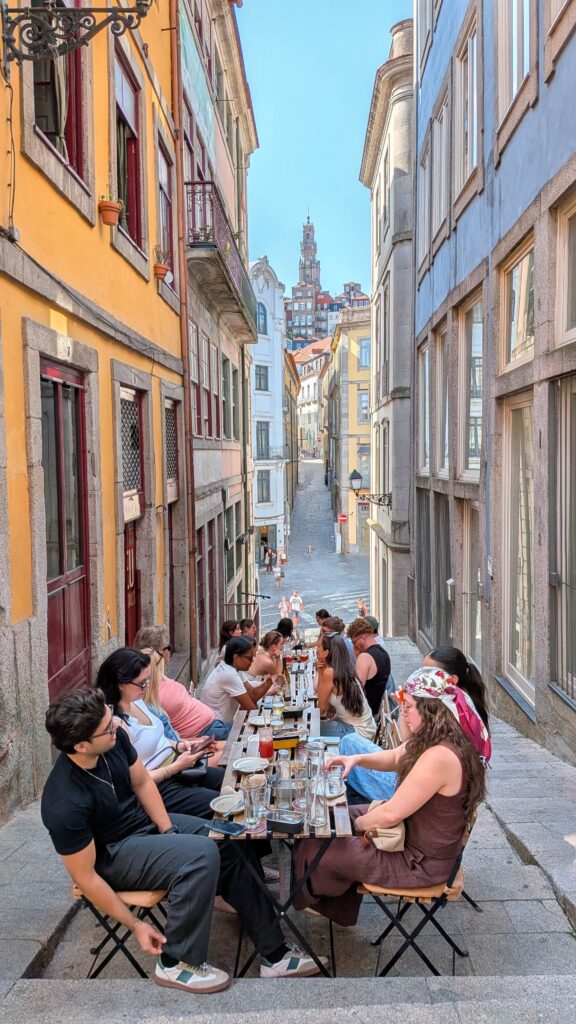 a group of young people sitting at a restaurant outside on one of porto's steep streets.